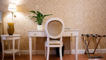 Een kamer met een wit bureau, een stoel, een kamerplant, een lamp en een bijzettafeltje met een vaas.