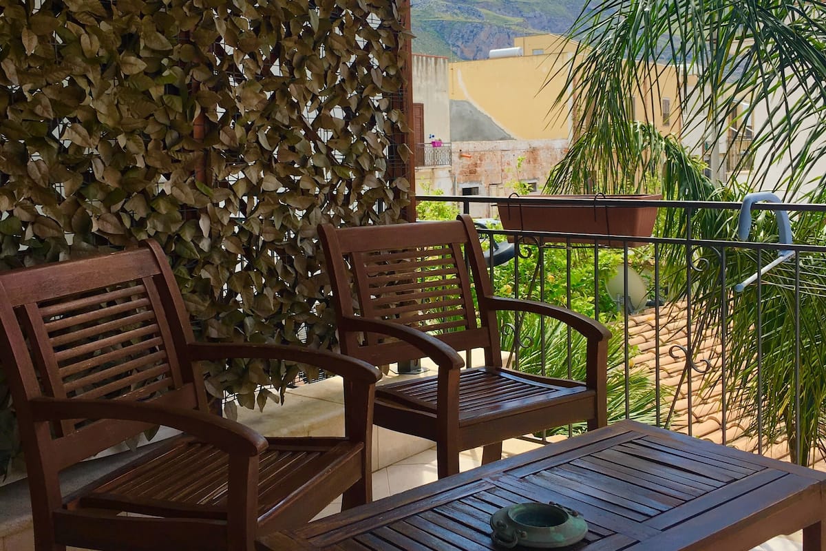 A wooden outdoor seating area with two chairs and a table, a lattice wall, and a view of mountains.