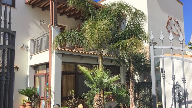 A courtyard with a patio table and chairs, surrounded by potted plants and a stone bench. - B&B Baglio Cusenza (San Vito Lo Capo)