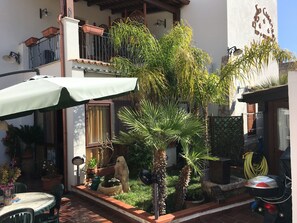 A courtyard with a table and chairs, potted plants, a motorcycle, and a building with a balcony. - B&B Baglio Cusenza (San Vito Lo Capo)
