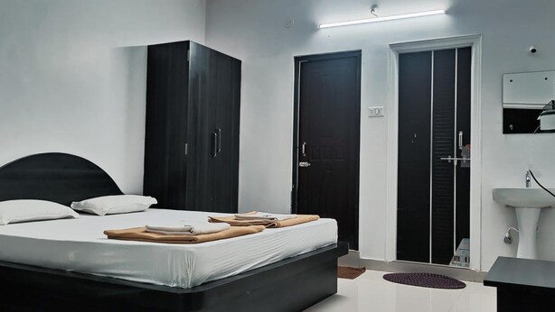 Un dormitorio moderno con cama, armario oscuro y baño con lavamanos y ducha.