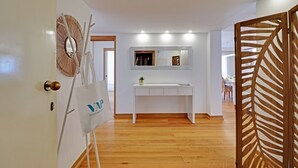 A hotel lobby with a wooden floor, a white reception desk, a mirror above the desk, and a decorative wall piece. - Home Out Luxury Marina Vilamoura (Quarteira)