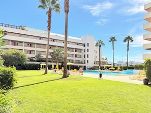 Un hôtel doté d’une piscine, de palmiers et de chaises longues.
