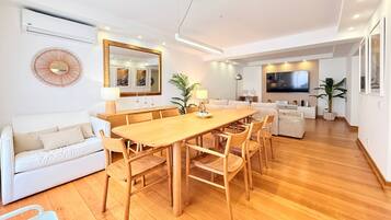 A modern living space with a dining area, sofa, and a TV mounted on the wall.