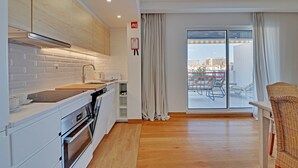 A modern kitchen with white cabinets, a built-in oven, and a large window with curtains. - Home Out Luxury Marina Vilamoura (Quarteira)