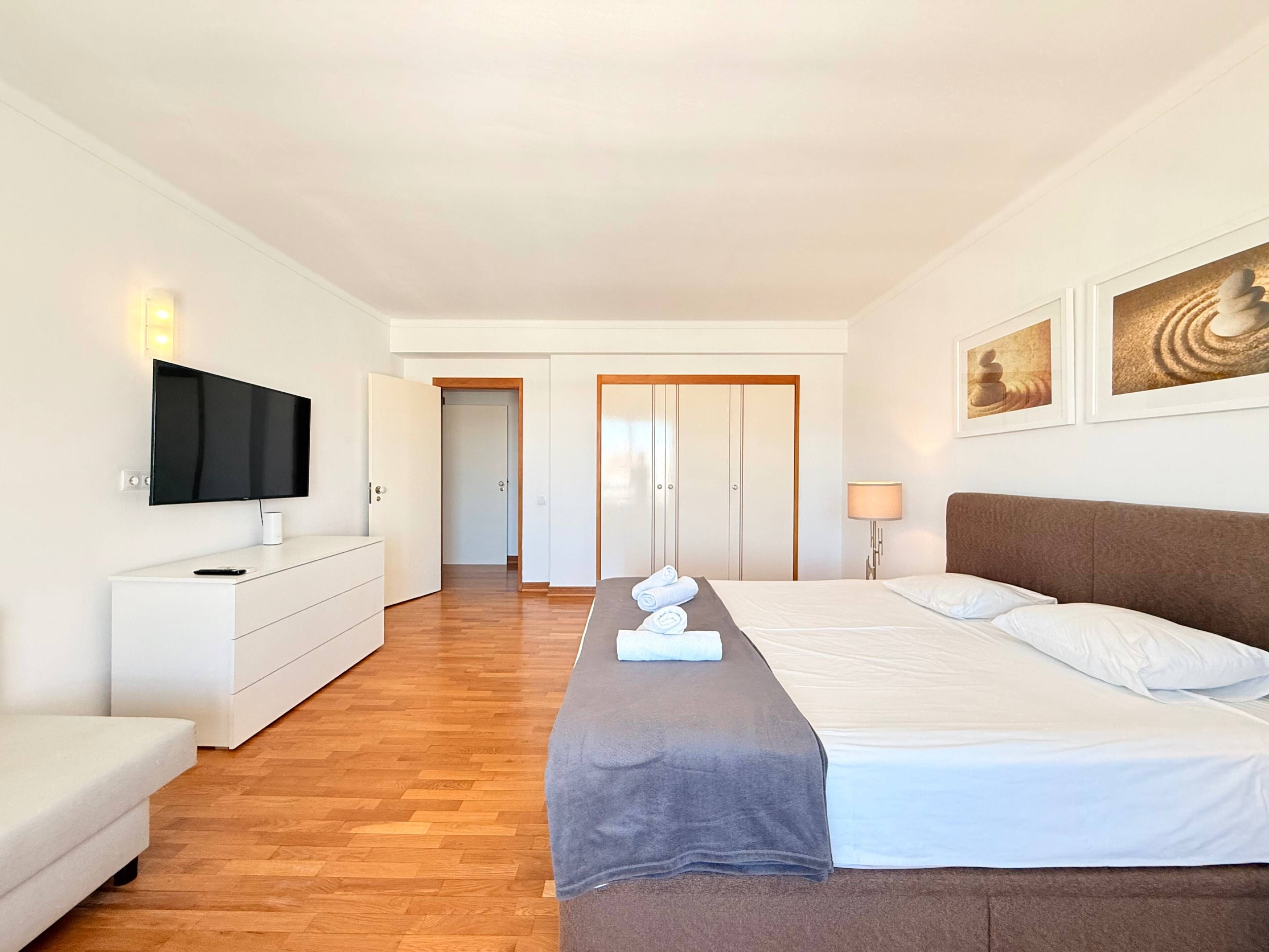 A hotel room with a bed, a TV, a dresser, and a door leading to another room.