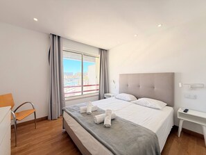 A hotel room with a bed, a chair, a bedside table, and a view of the city.