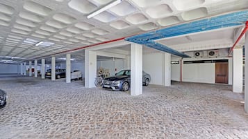 Eine überdachte Tiefgarage mit mehreren Parkreihen, weißen Säulen und einem Kopfsteinpflasterboden.