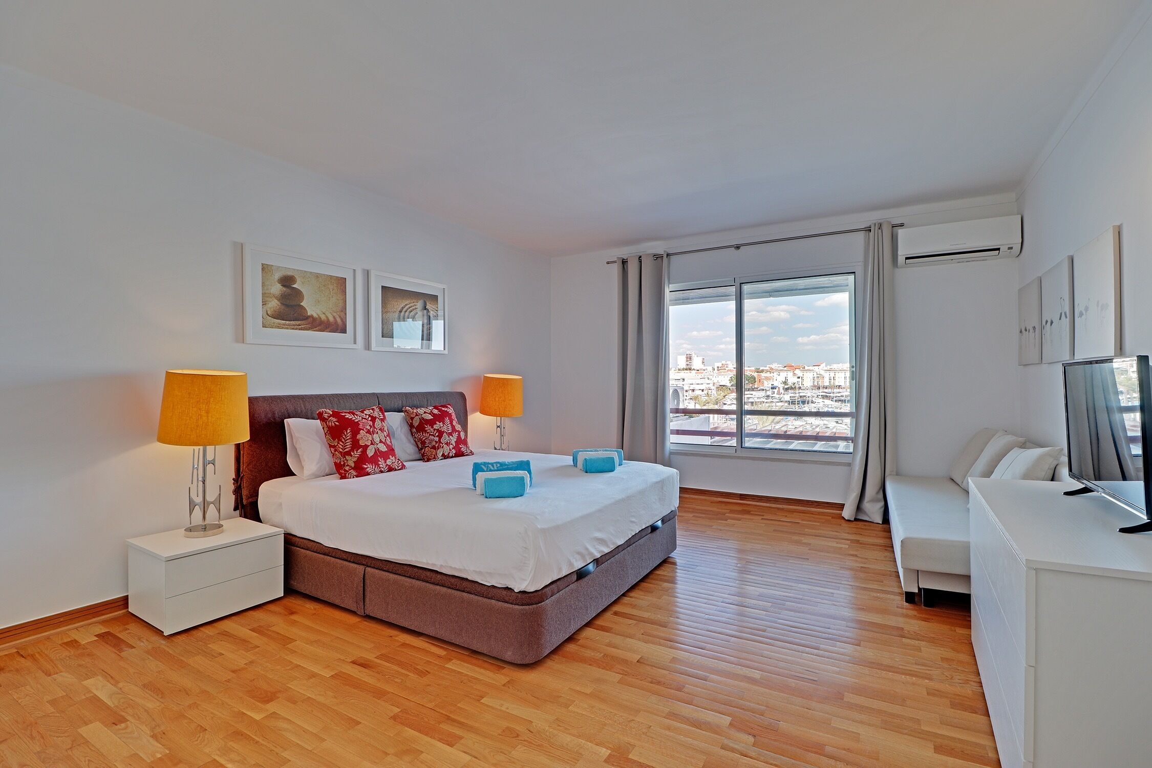 Une chambre d’hôtel moderne, dotée d’un grand lit, de lampes de chevet, d’une télévision et offrant une vue sur la ville par la fenêtre.