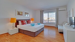 A modern hotel room with a large bed, bedside lamps, a TV, and a view of the city through the window. - Home Out Luxury Marina Vilamoura (Quarteira)