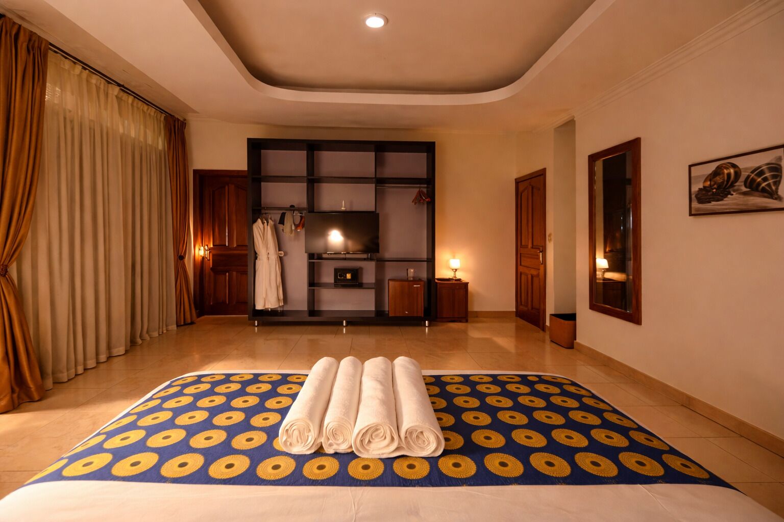 A hotel room with a large bed, a built-in TV, a wardrobe, and a bathroom visible through a glass door.
