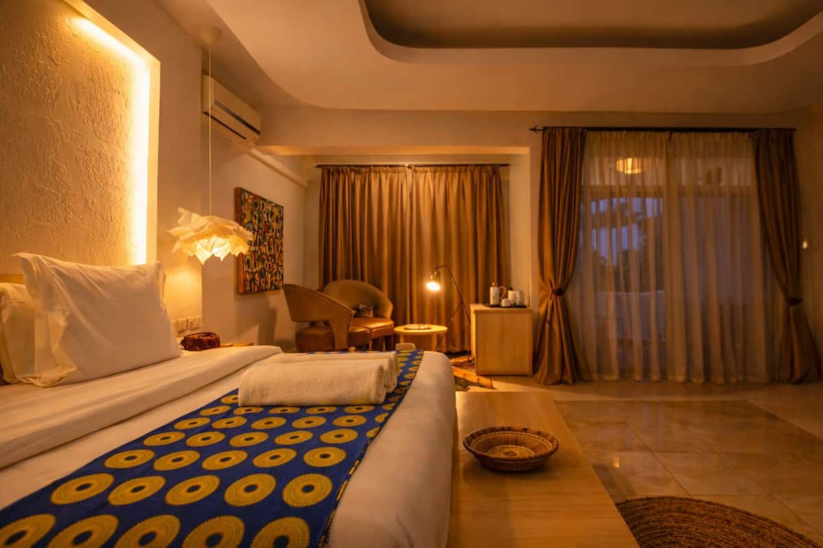 Ein Hotelzimmer mit Bett, Schreibtisch, Stuhl, Lampe, einem Vorhangfenster und einer Wandklimaanlage.