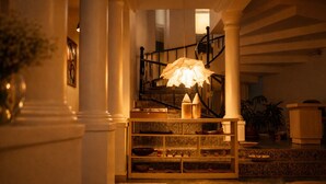Un escalier orné d’un lustre, une étagère en bois avec divers objets, et une plante en pot.