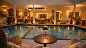 Un espace aménagé au bord de la piscine, avec des chaises longues, une table avec une lampe et un coin repas avec des tables et des chaises.