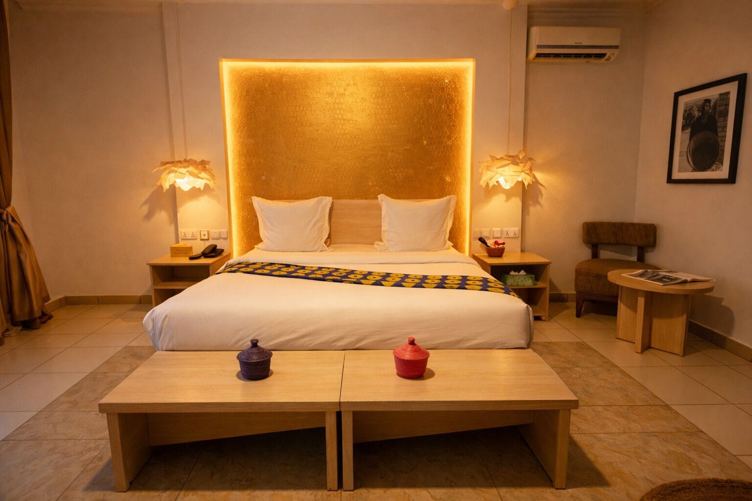 A hotel room with a large bed, bedside lamps, a small table, a chair, and a framed picture on the wall.