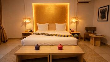 A hotel room with a large bed, bedside lamps, a small table, a chair, and a framed picture on the wall.