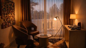 Une chambre d’hôtel avec un canapé, une petite table ronde, une lampe, un coin café et une grande fenêtre avec des rideaux.