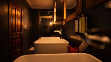 A narrow hallway leading to a bathroom with a white sink, a wooden door, and a mirror.
