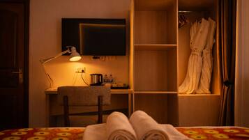 Habitación de hotel con cama, escritorio con lámpara, televisor, armario y una toalla sobre la cama.