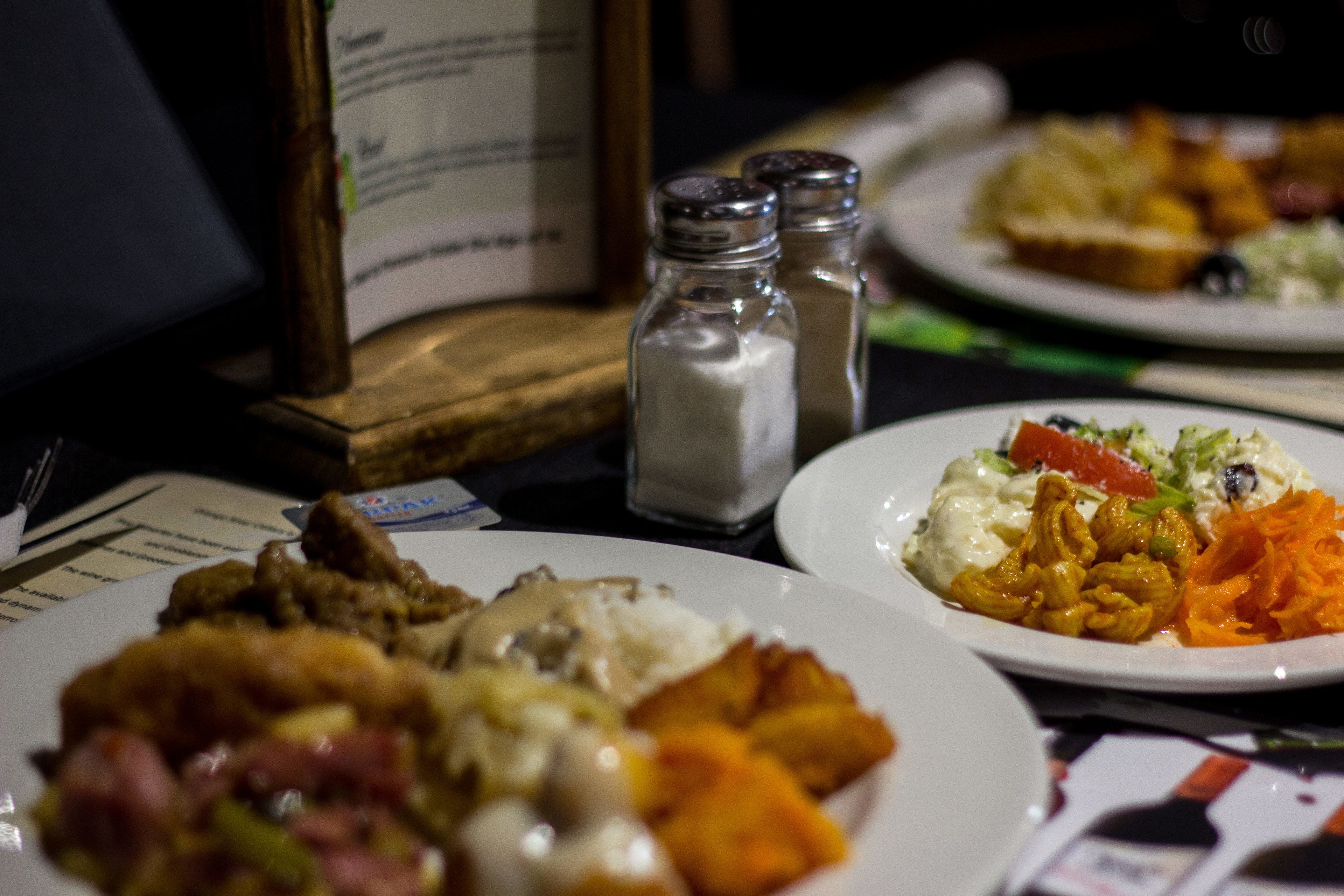 Una mesa de comedor con platos de comida, saleros y pimenteros, y una carta.