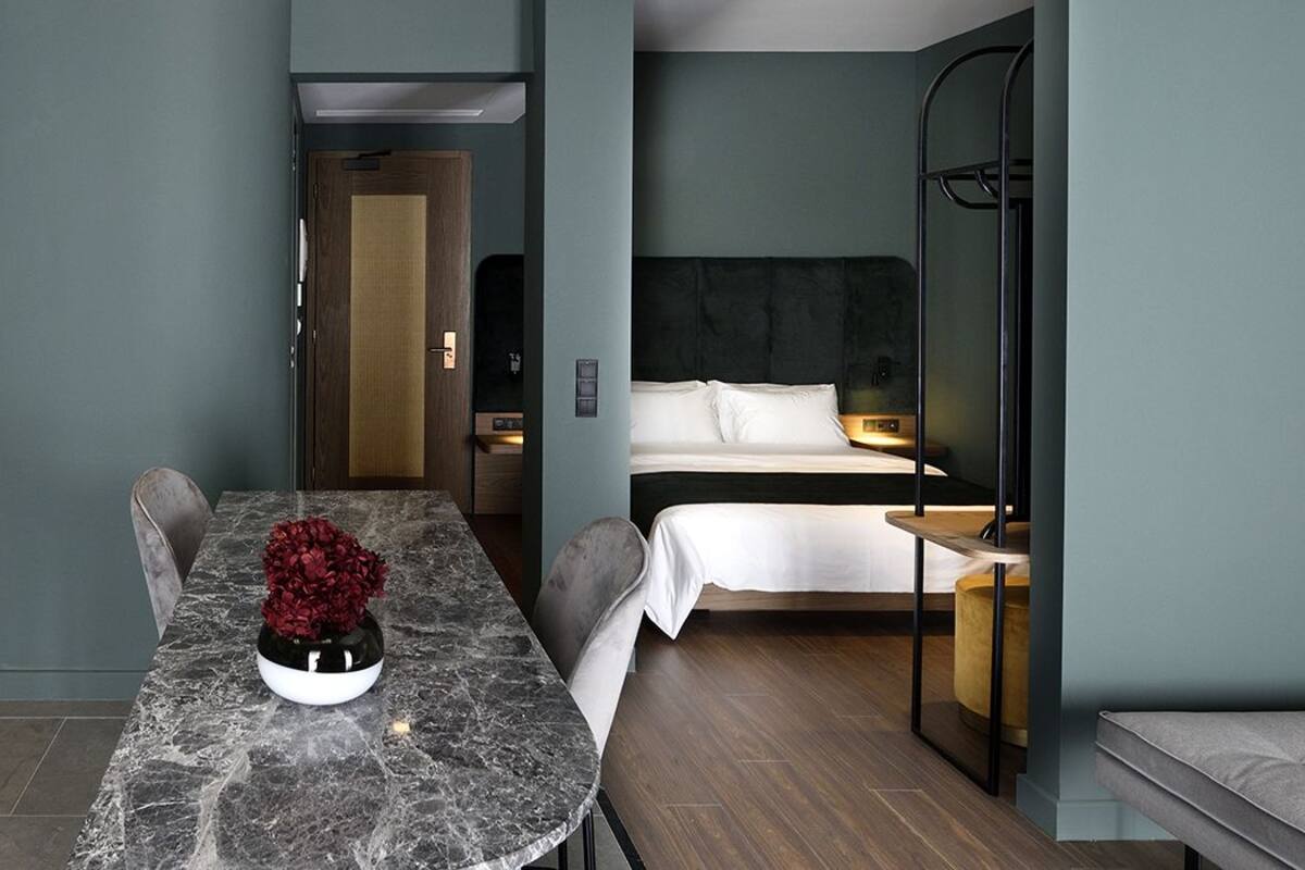 Une chambre d’hôtel compacte, dotée d’une kitchenette, d’un lit avec du linge de lit blanc et d’un petit coin salon.