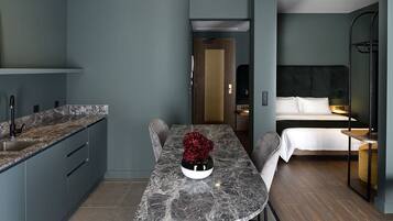Una habitación de hotel compacta con kitchenette, una cama con ropa blanca y un pequeño rincón de descanso.