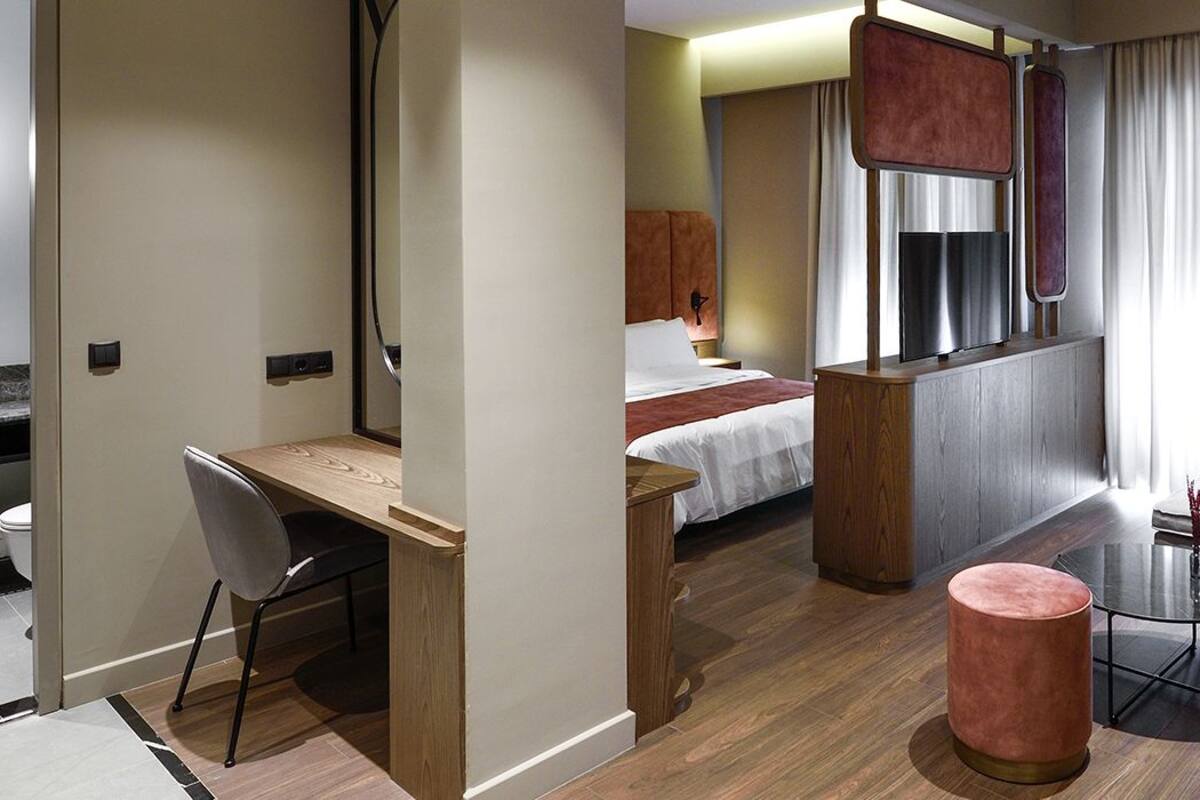 Une chambre d’hôtel comprenant un lit, un bureau, une chaise, une petite table, un canapé et une fenêtre avec des rideaux.