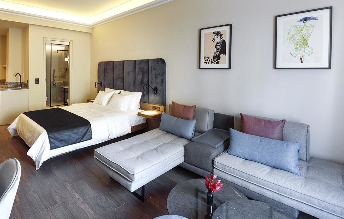 A modern hotel room with a large bed, a sofa, and a small table with a vase.