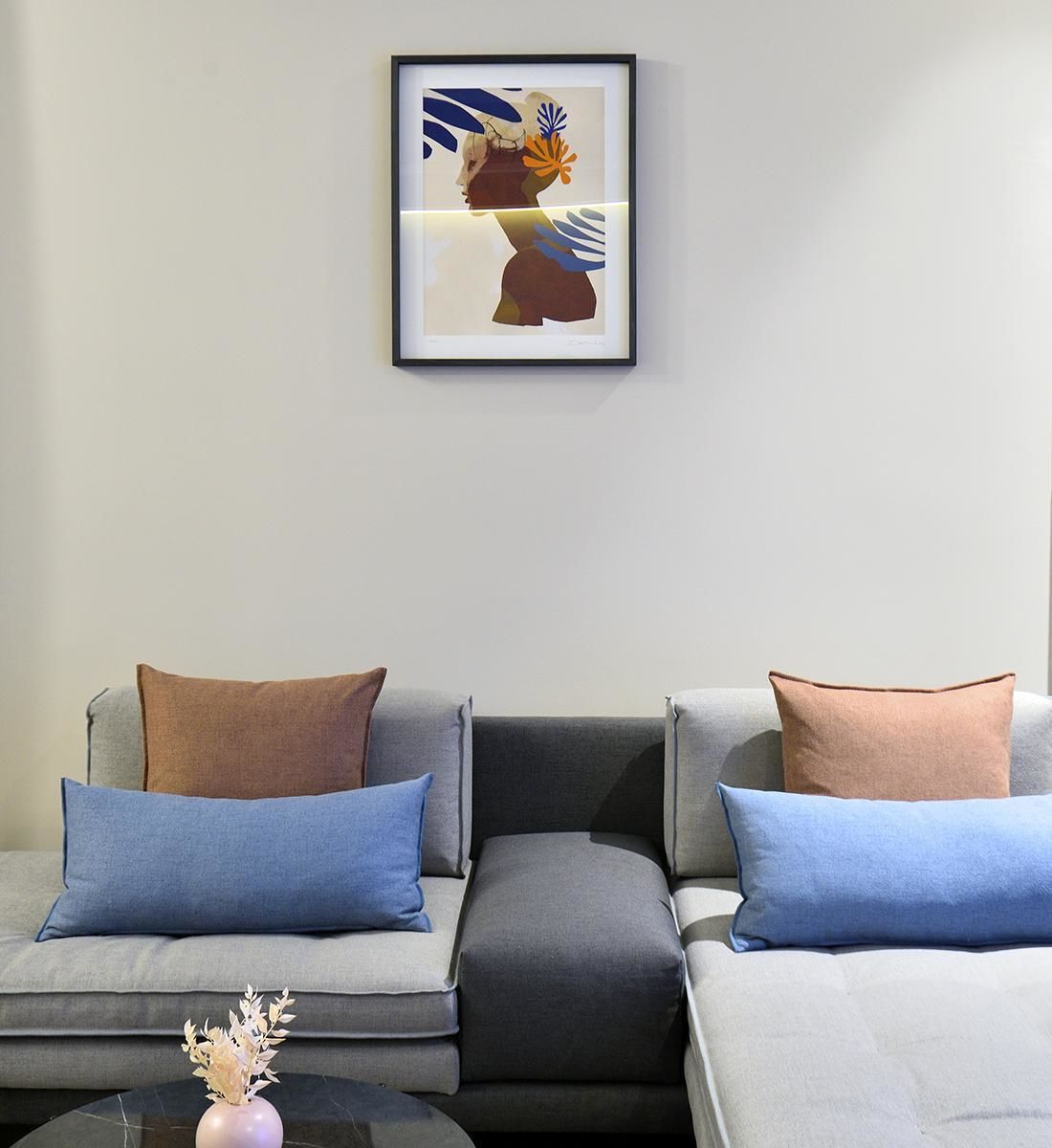 Una sala de estar moderna con un sofá gris, cojines azules y marrones, y una obra de arte abstracta enmarcada en la pared.