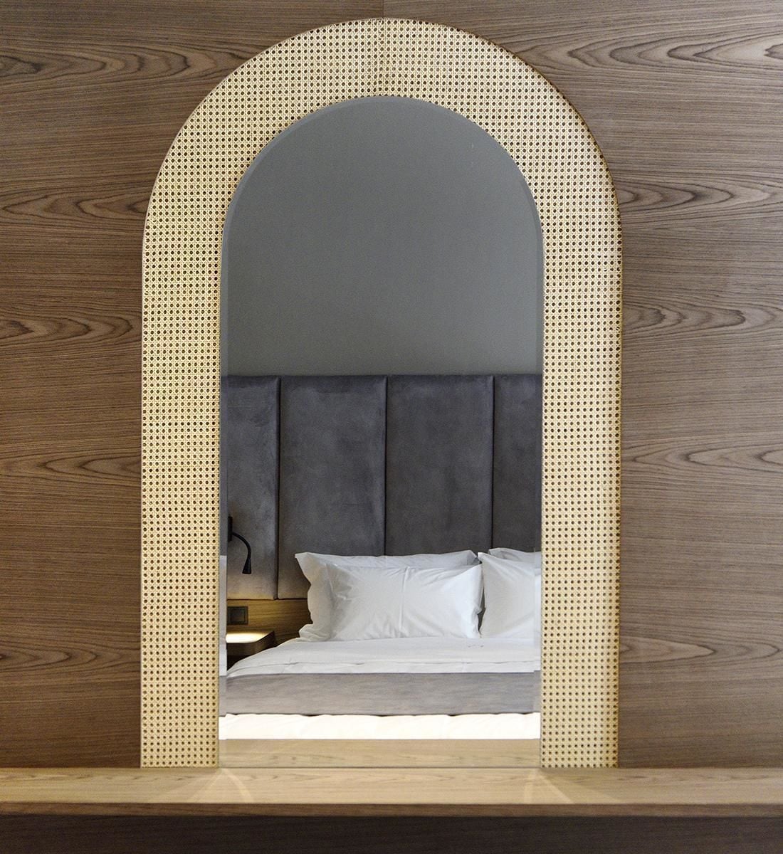 Una cama con cabecera tapizada en gris, ropa de cama blanca y piso de madera.