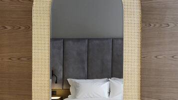 Una cama con cabecera tapizada en gris, ropa de cama blanca y piso de madera.
