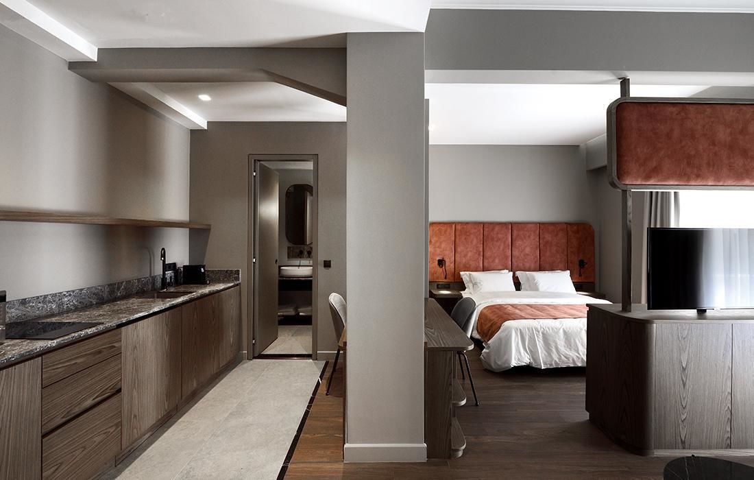 Ein modernes Hotelzimmer mit einer Küchenzeile, einem Bett mit Kopfteil und einem Fernseher.
