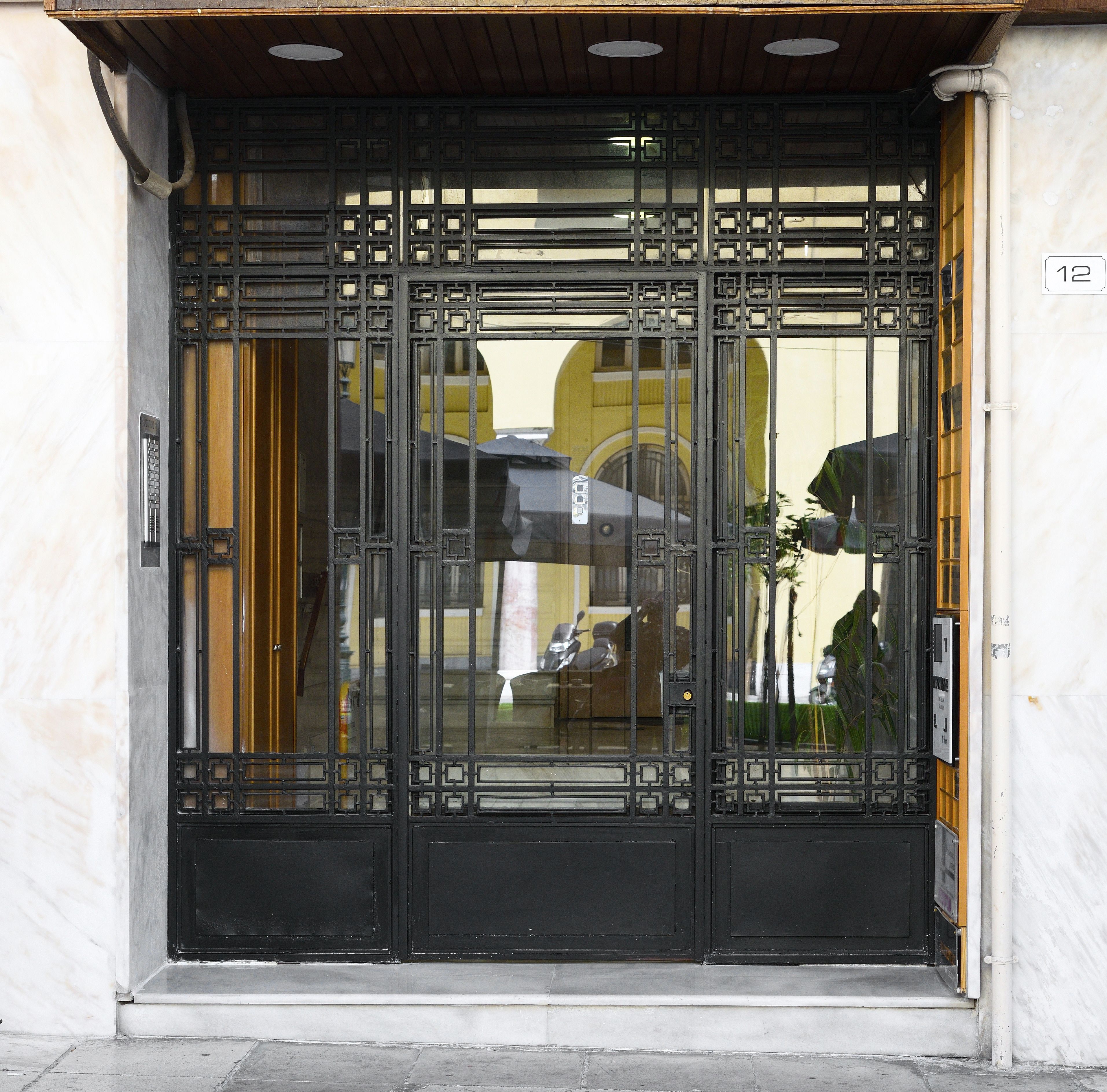 A black metal gate with intricate designs, a yellow door frame, and a white wall.