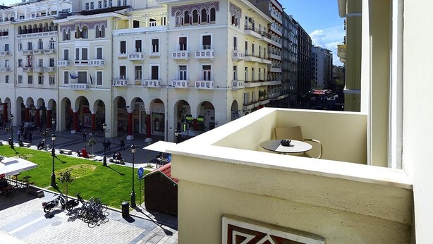 A balcony with a geometric design, overlooking a street with buildings and a green area. - Roomore Apartments (Thessaloniki)