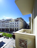 Ein Balkon mit geometrischem Design, der auf eine Straße mit Gebäuden und einer Grünfläche blickt.