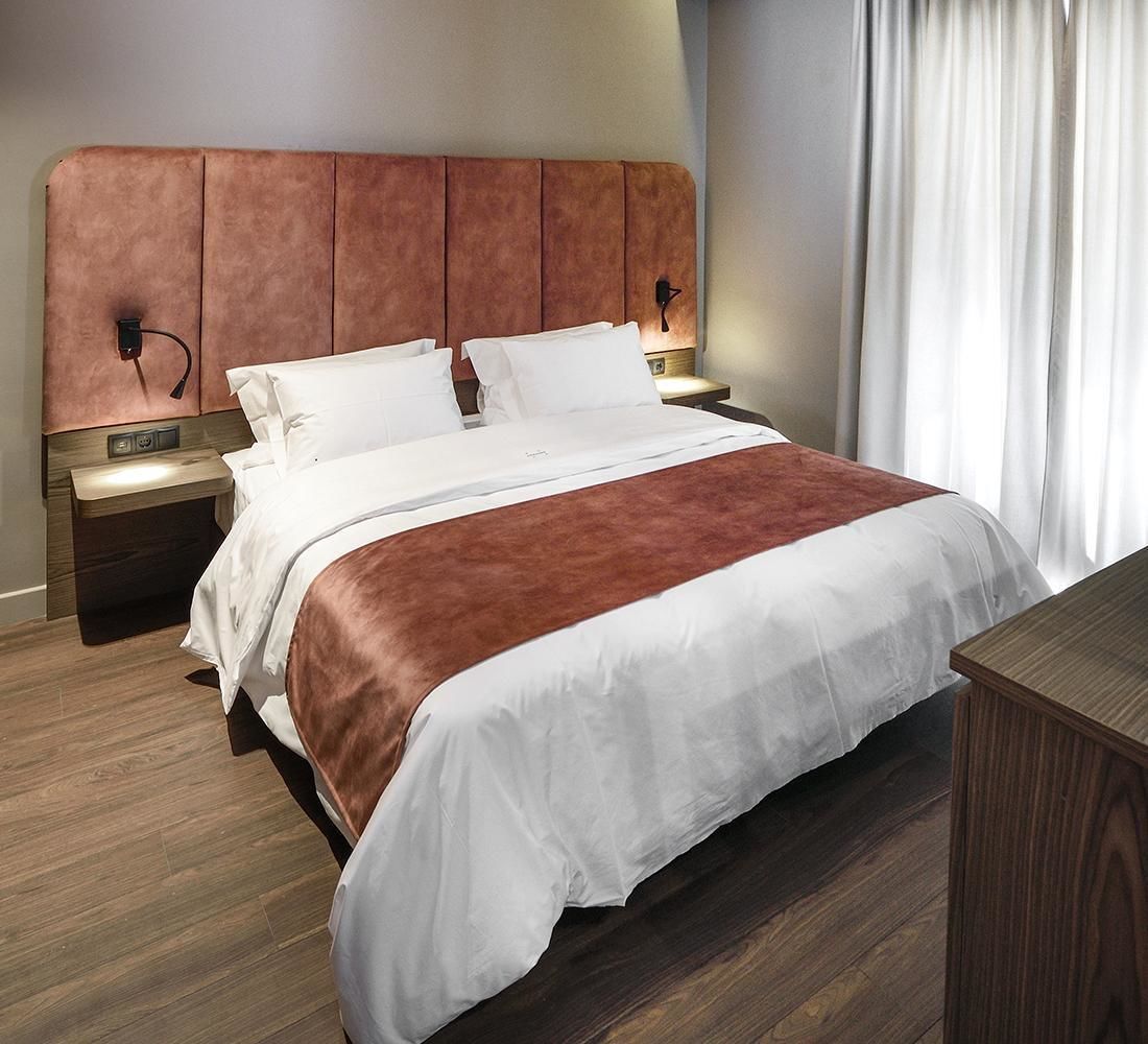 A hotel room with a large bed, wooden headboard, two bedside tables, and a nightstand.