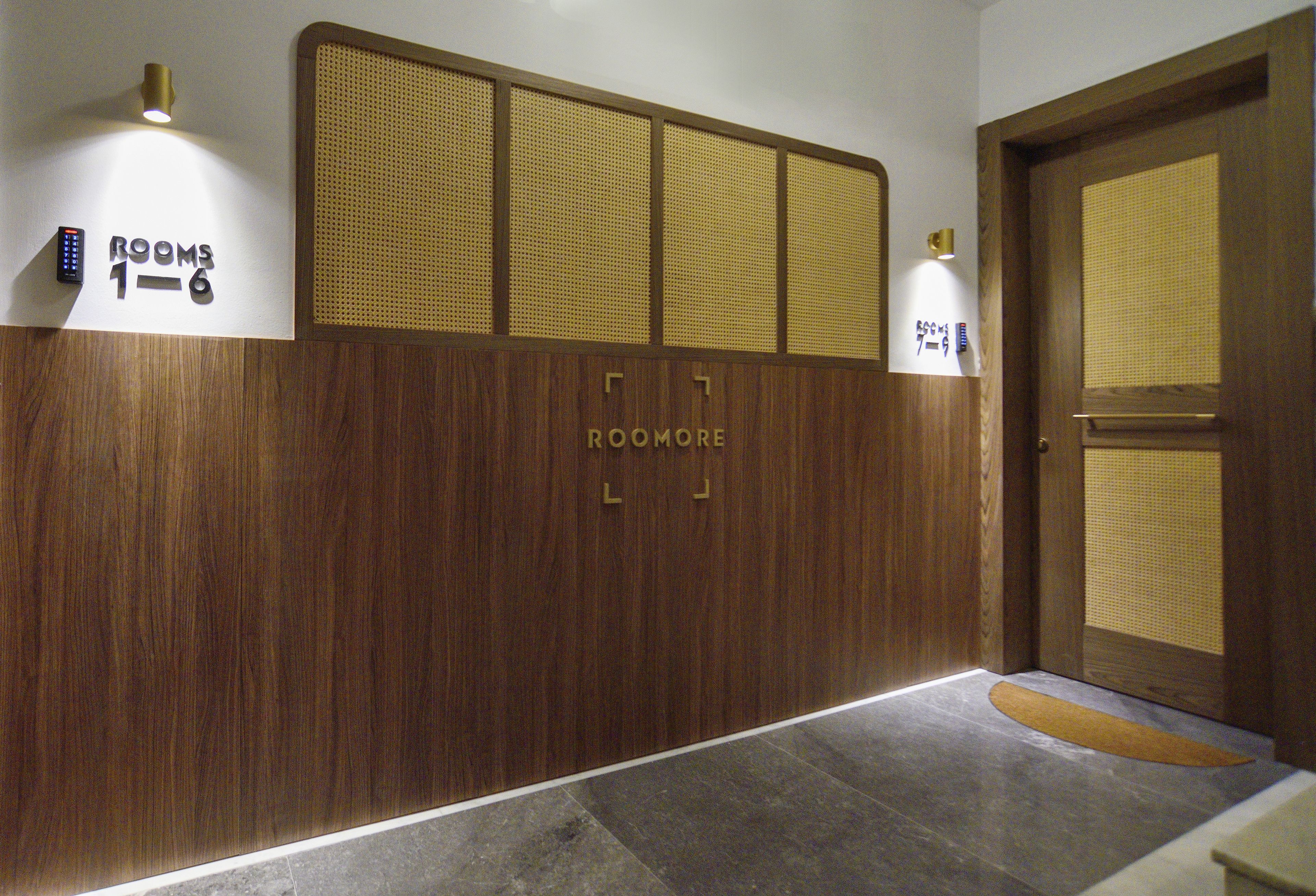 Un pasillo con pared de madera, un cartel que indica las habitaciones 1 a 6, y una puerta con celosía tejida.