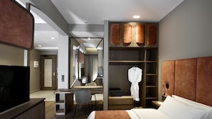 A hotel room with a bed, a desk, a chair, a wardrobe, and a television. - Roomore Apartments (Thessaloniki)