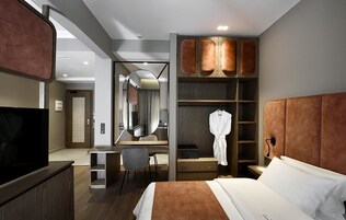A hotel room with a bed, a desk, a chair, a wardrobe, and a television.