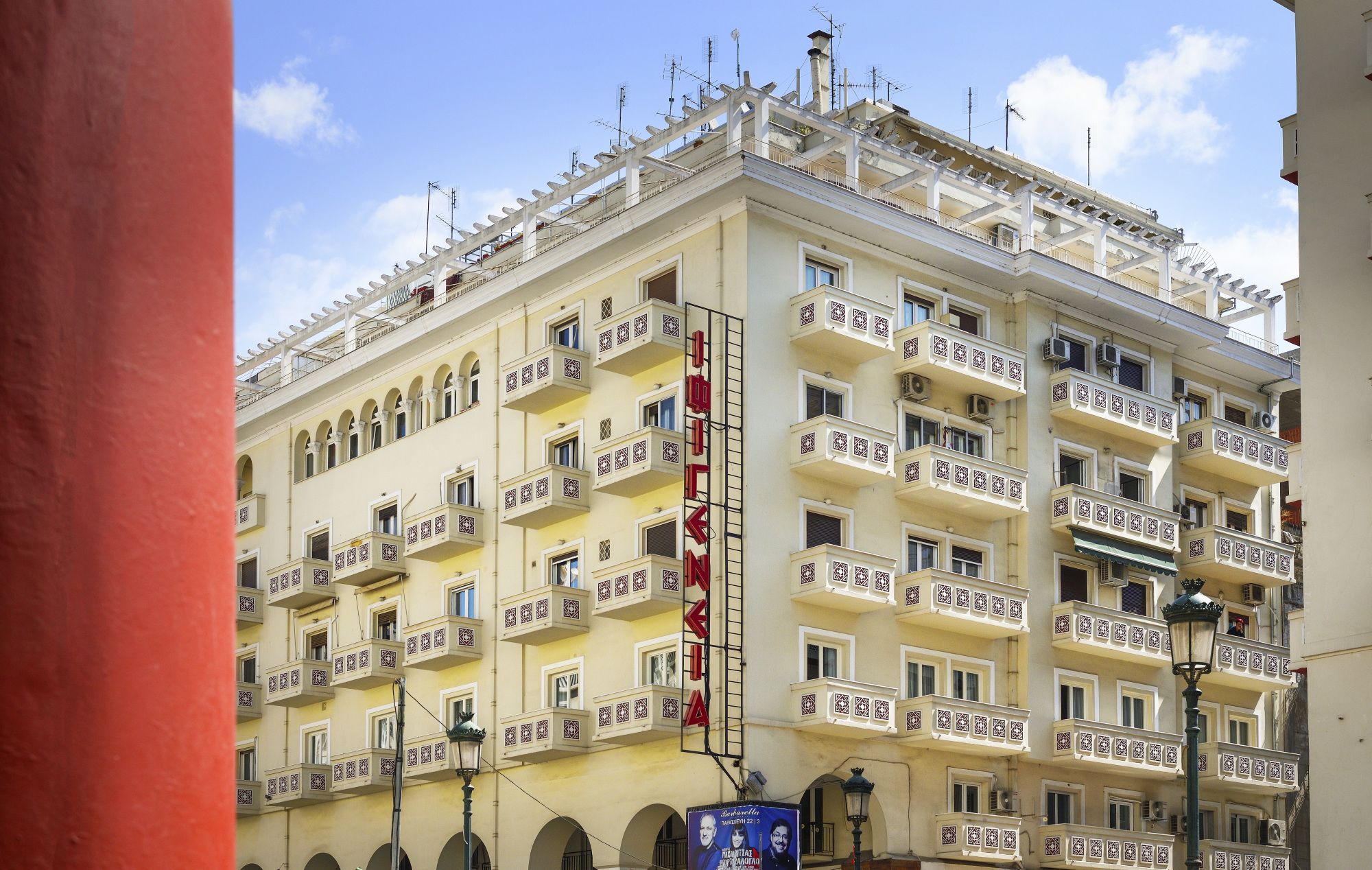 A multi-story hotel with balconies, a prominent red sign, and a clear sky.
