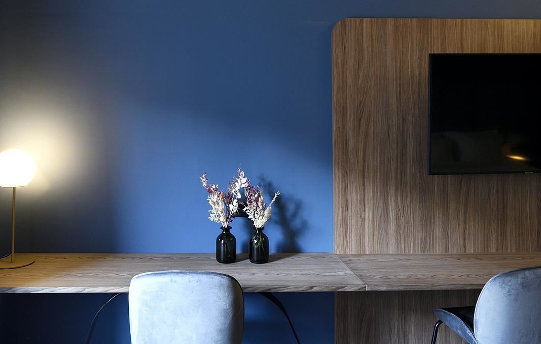 A modern room with a wooden desk, two chairs, a lamp, and a flat-screen TV mounted on a wooden wall.
