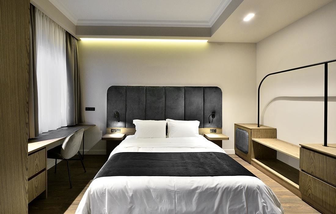 Une chambre d’hôtel moderne avec un grand lit, un bureau et une chaise. Il y a deux tables de chevet avec des lampes.