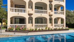 Un hotel de varios pisos con balcones, piscina y un jardín con flores rosadas.