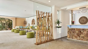 Una moderna recepción con mostrador de piedra, asientos verdes y un panel decorativo de madera.