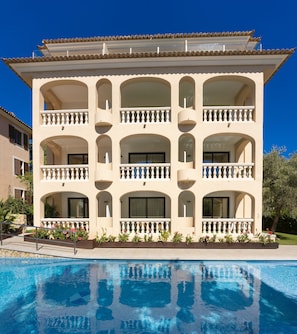 A multi-story hotel with balconies, a swimming pool, and a clear blue sky. - Apartamentos s'Olivera (Capdepera)