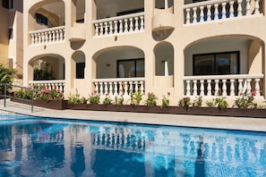A hotel with a swimming pool, balconies with white railings, and flower beds. - Apartamentos s'Olivera (Capdepera)