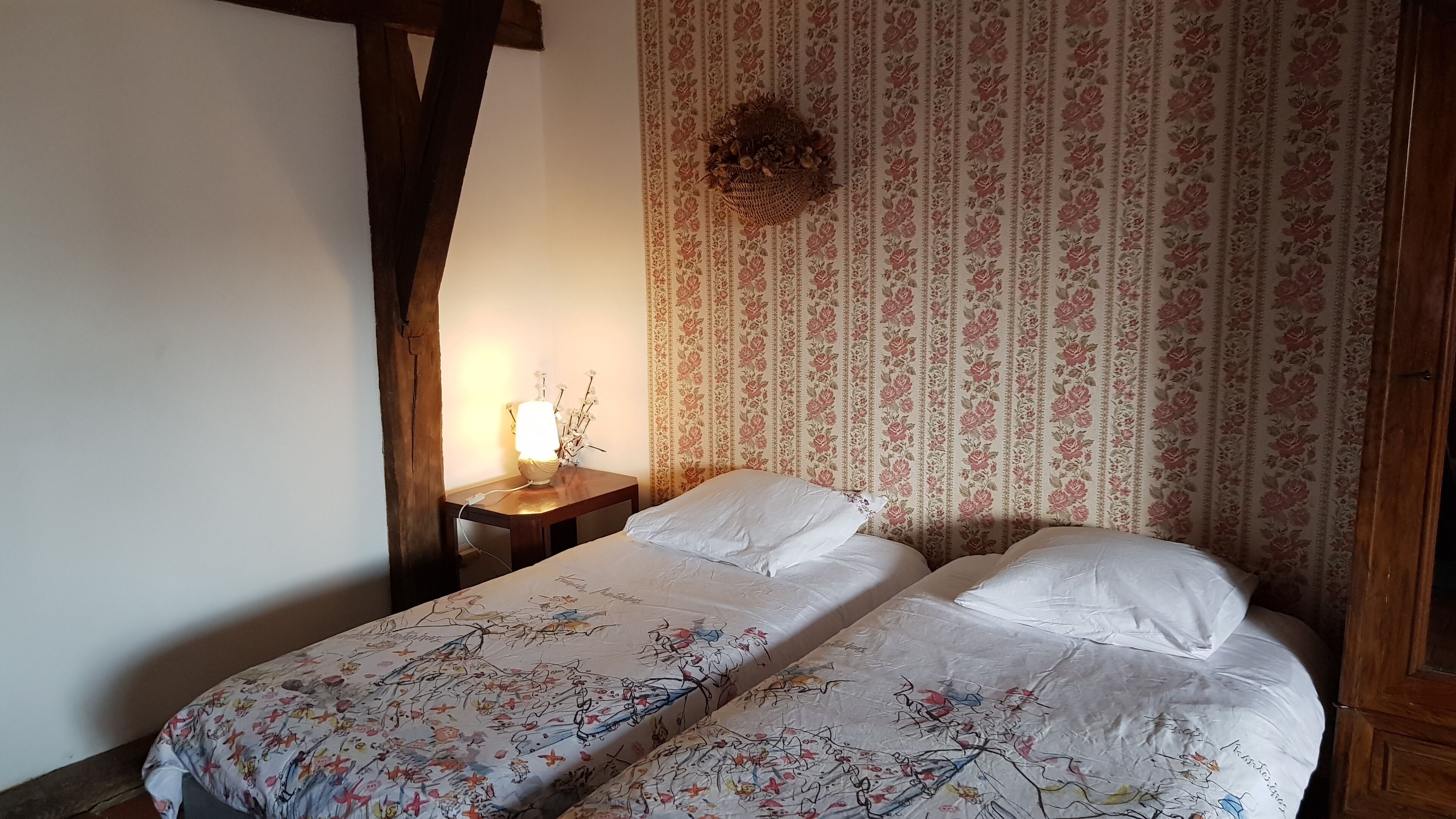 Une chambre avec deux lits, un papier peint à motifs floraux, une table de chevet avec une lampe et une décoration murale.