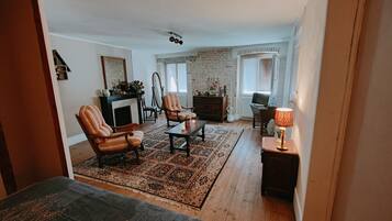 Un salon chaleureux avec une cheminée, deux fauteuils, une table basse et un ordinateur portable posé sur un bureau.