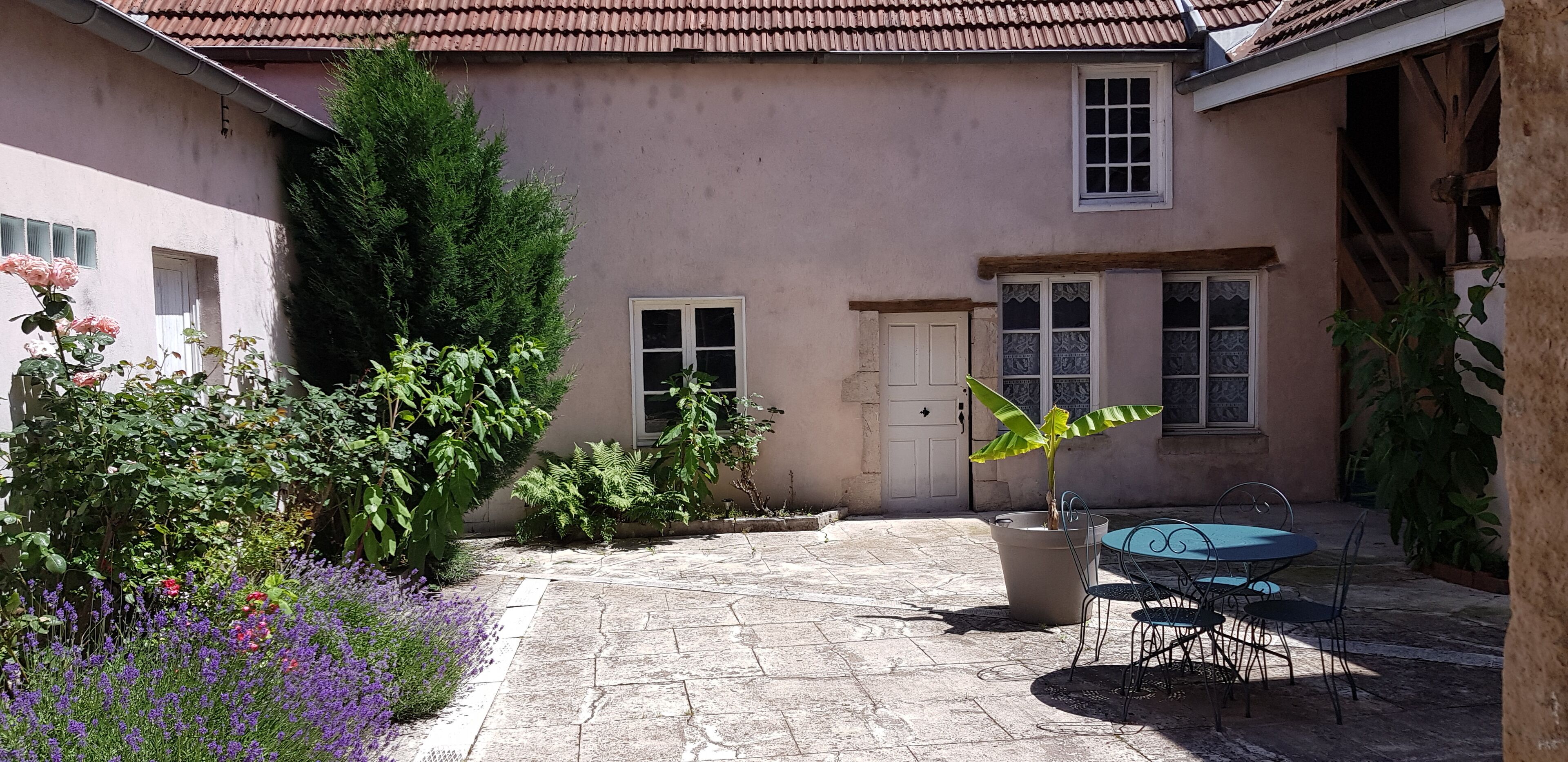 A courtyard with a stone floor, a table with chairs, and a potted plant.