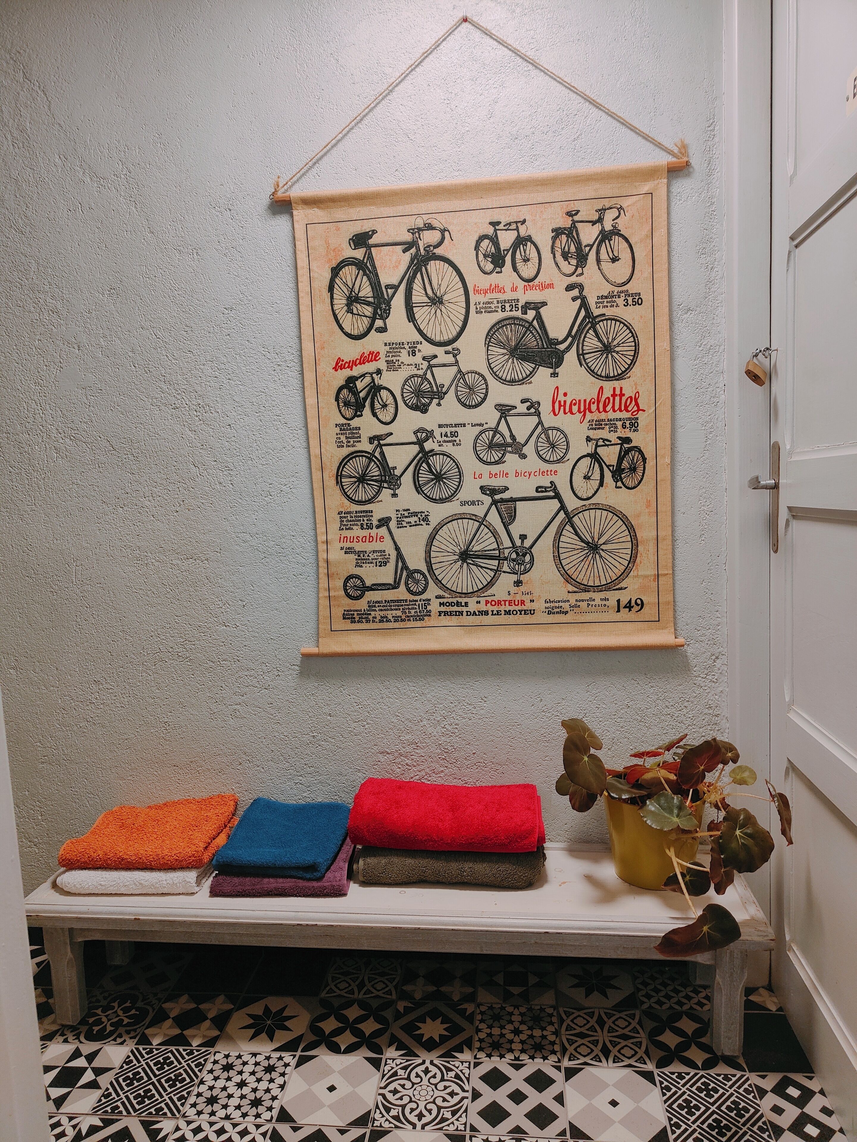 Een hal met een fiets-poster aan de muur, een bank met kleurrijke handdoeken en een vloer van versierde tegels.